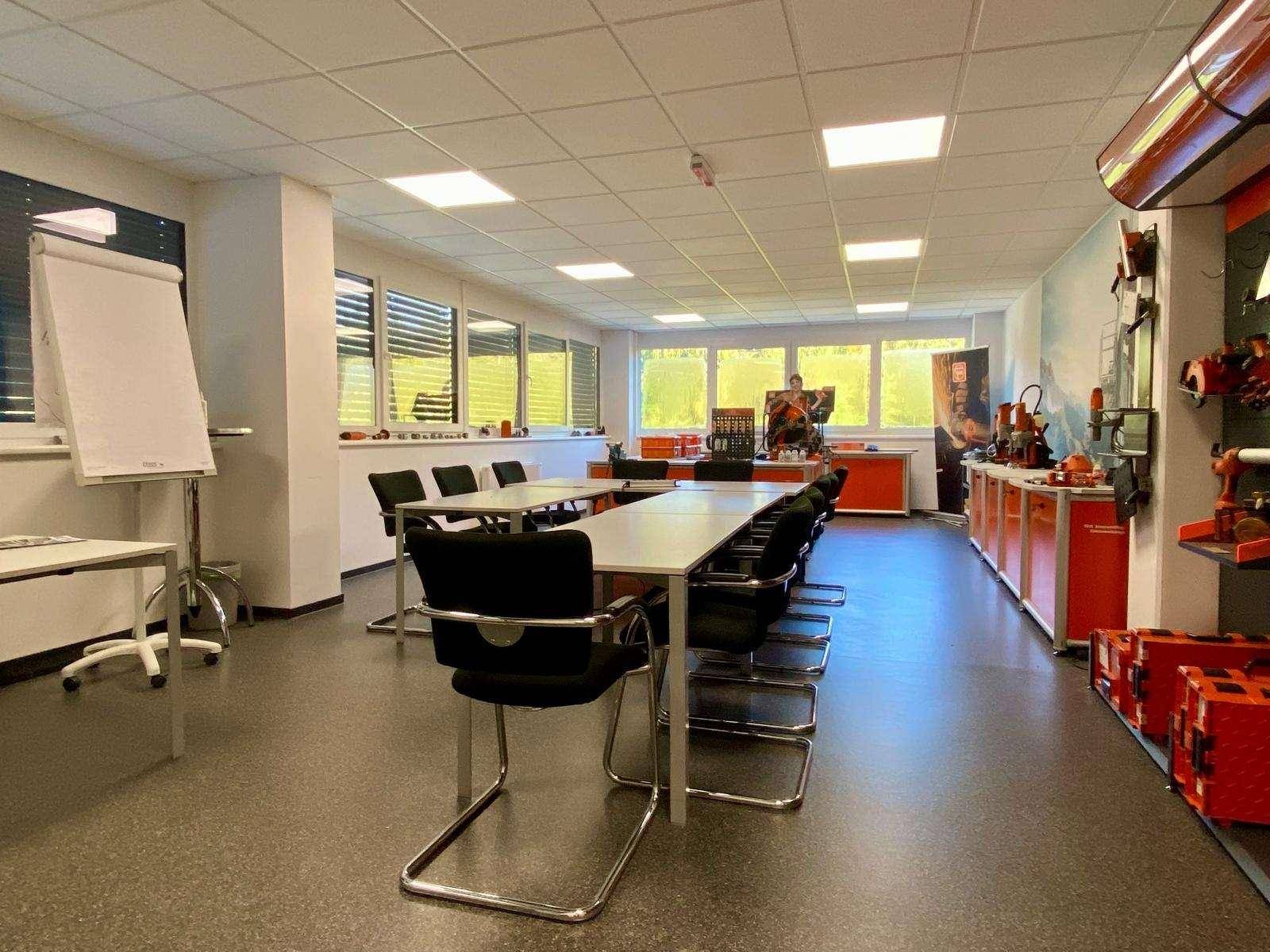 Heller Konferenzraum mit mehreren Tischen, Stühlen und einem Whiteboard, ideal für Schulungen und Besprechungen.