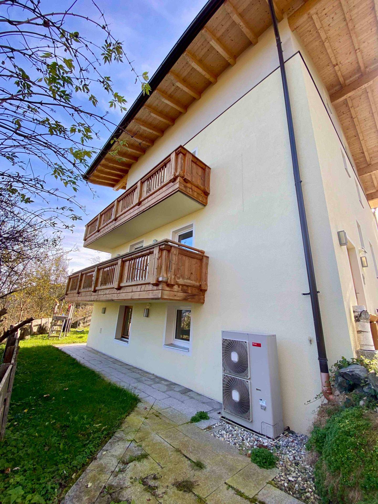 Seitenansicht des Hauses mit Balkonen und einer Wärmepumpe an der Fassade.