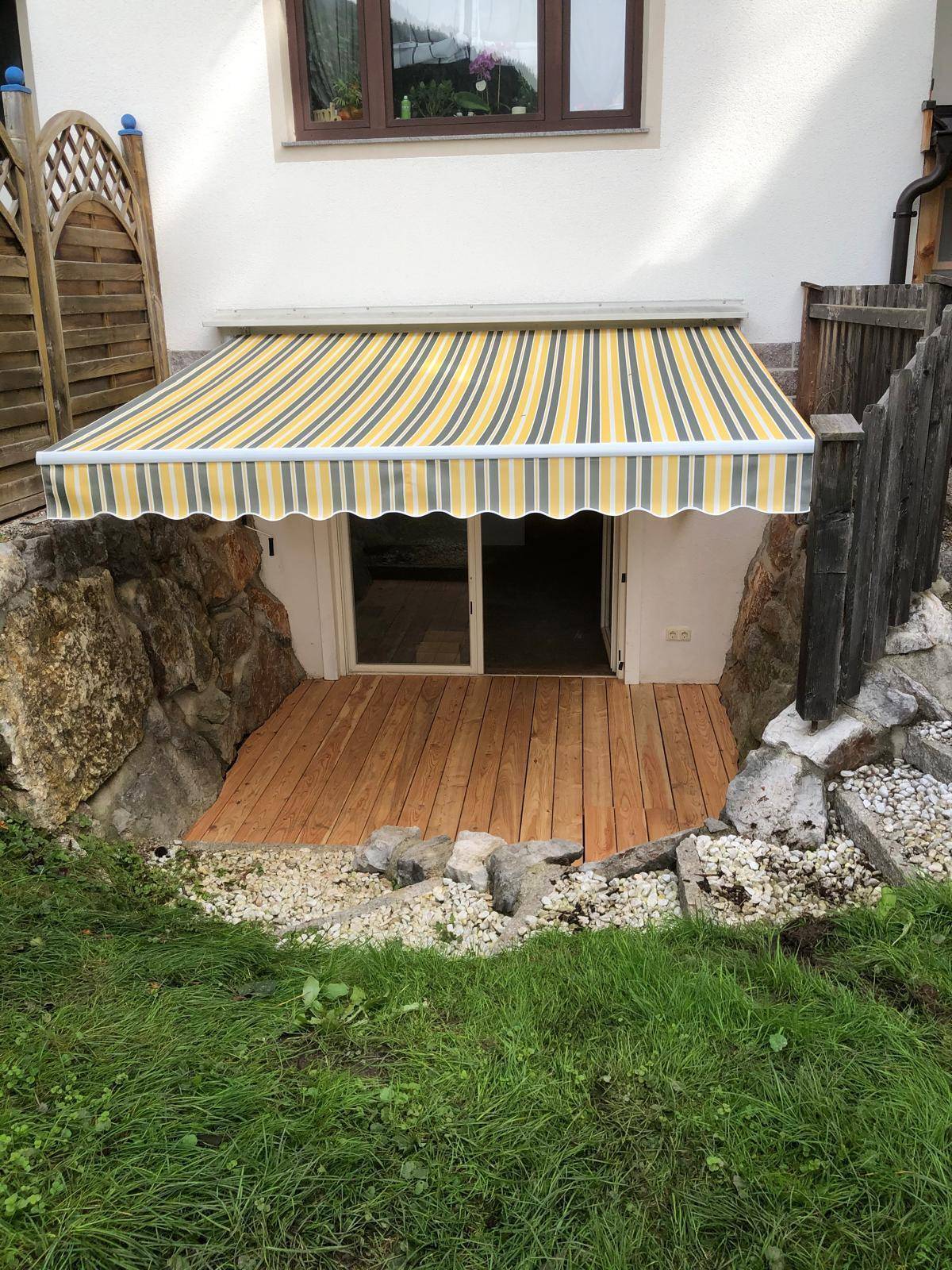 Gemütliche Terrasse im Untergeschoss mit Holzdeck, Markise und Zugang zum Innenbereich.