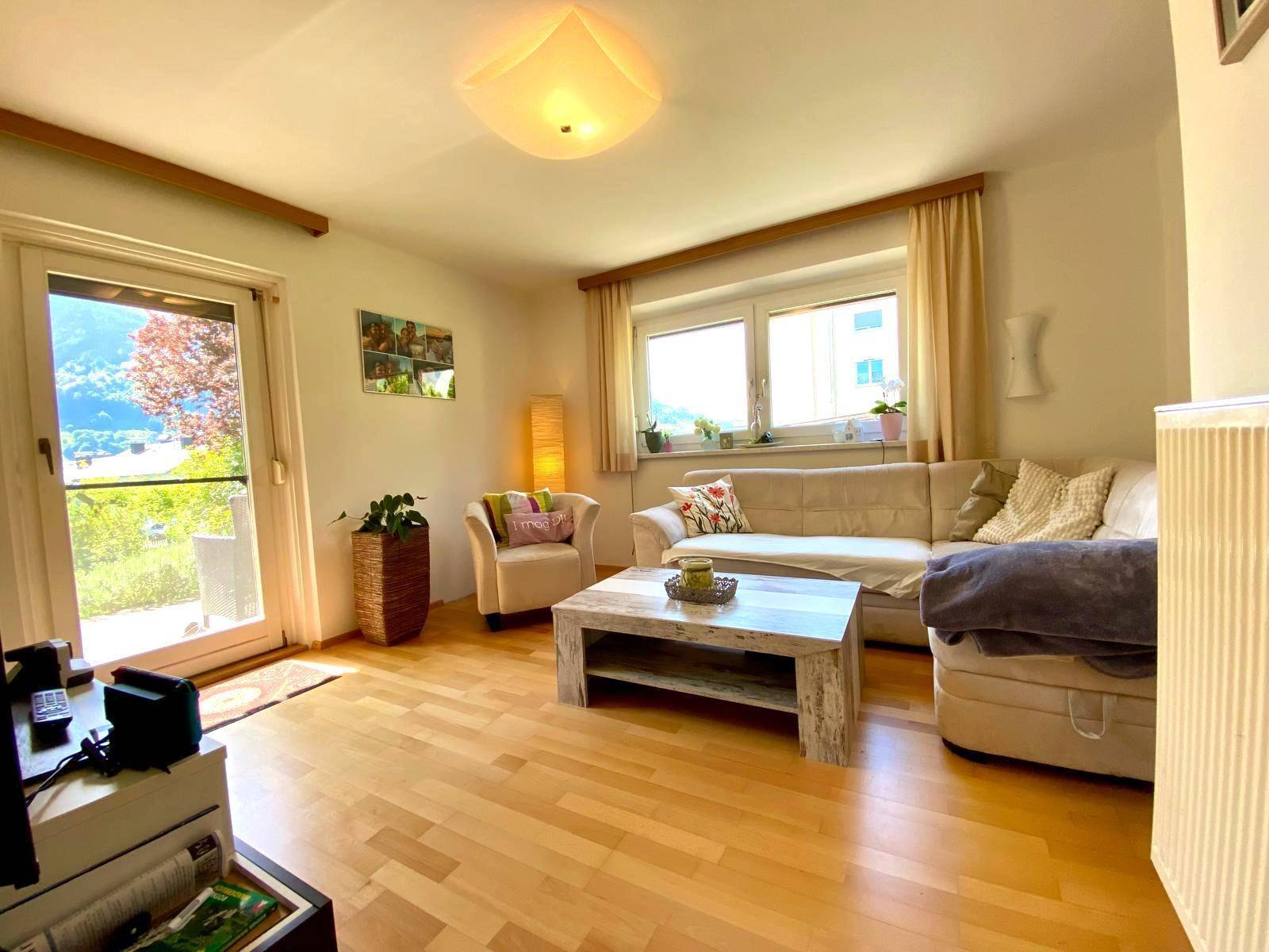 Helles Wohnzimmer mit beigem Sofa, Holzboden und Zugang zu einem Balkon.