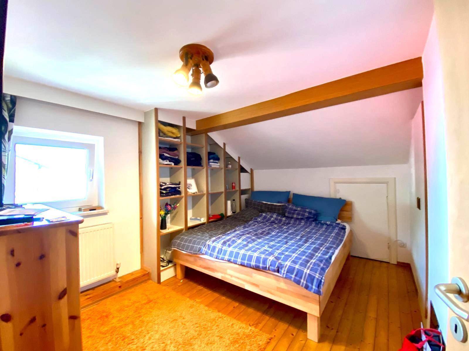 Gemütliches Schlafzimmer im Dachgeschoss mit Holzbett, Einbauregalen und Schrägen.