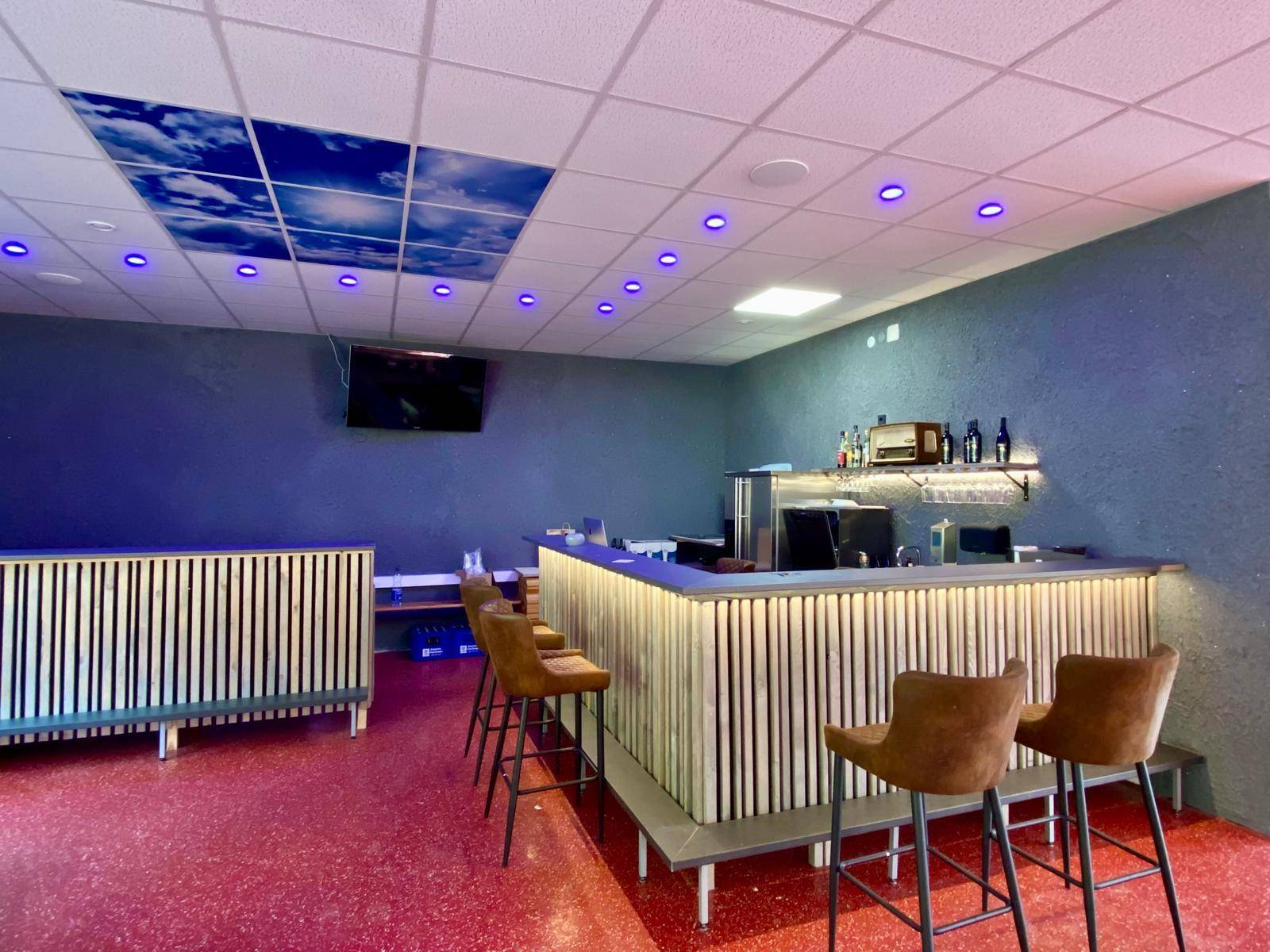 Detailansicht der modernen Bar mit Hockern, Flaschenregal und Deckenbeleuchtung, funktional und stilvoll.