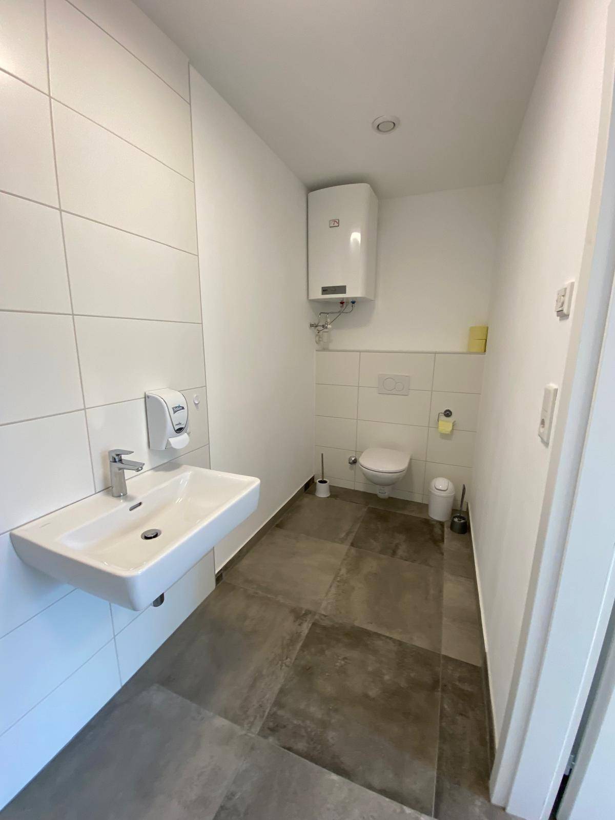 Saubere Toilette mit wandhängendem WC, Waschbecken und weiß-grauen Fliesen, in gutem Zustand.