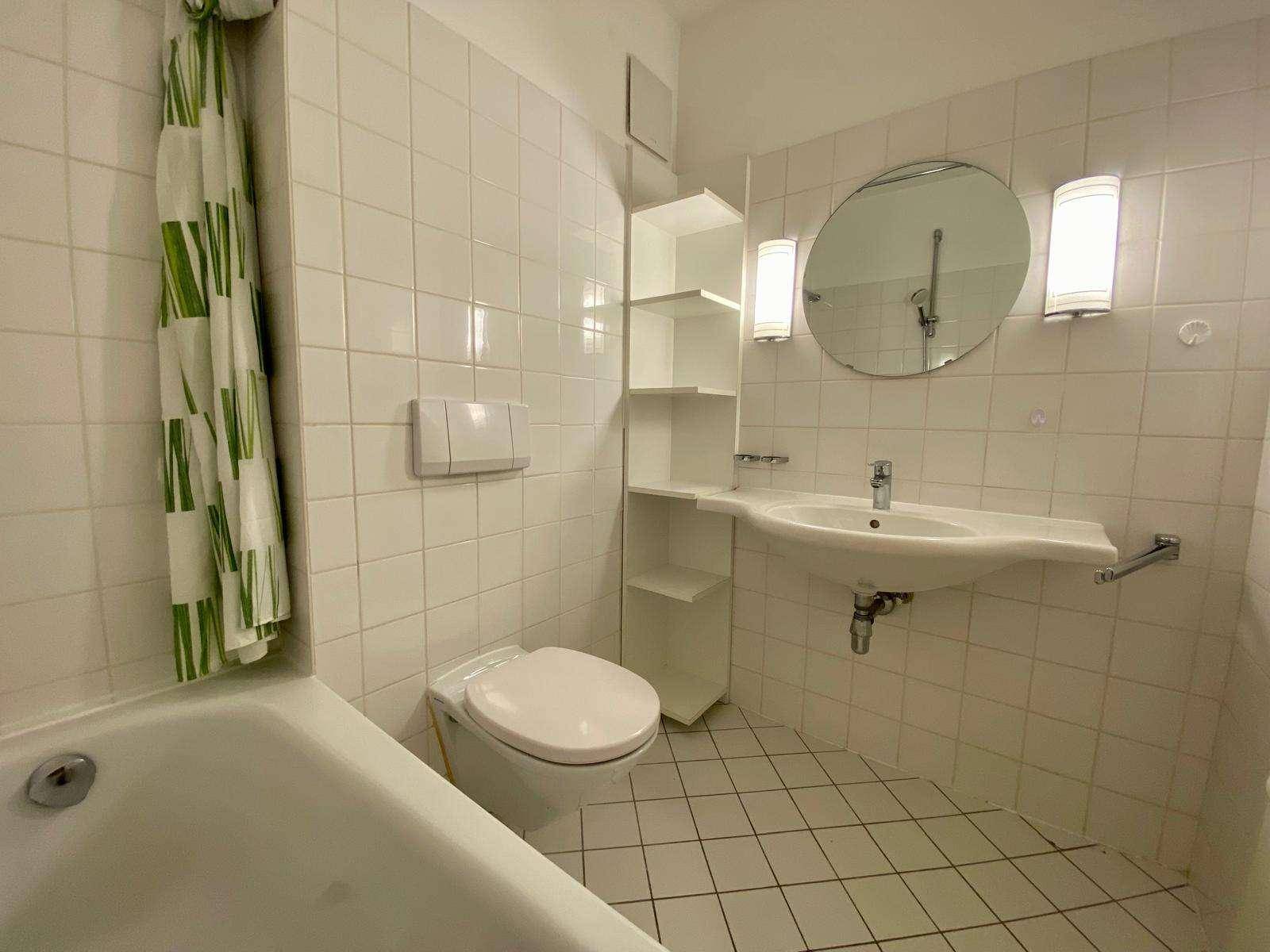 Helles Badezimmer mit weißen Fliesen, Badewanne mit Duschvorhang und WC.