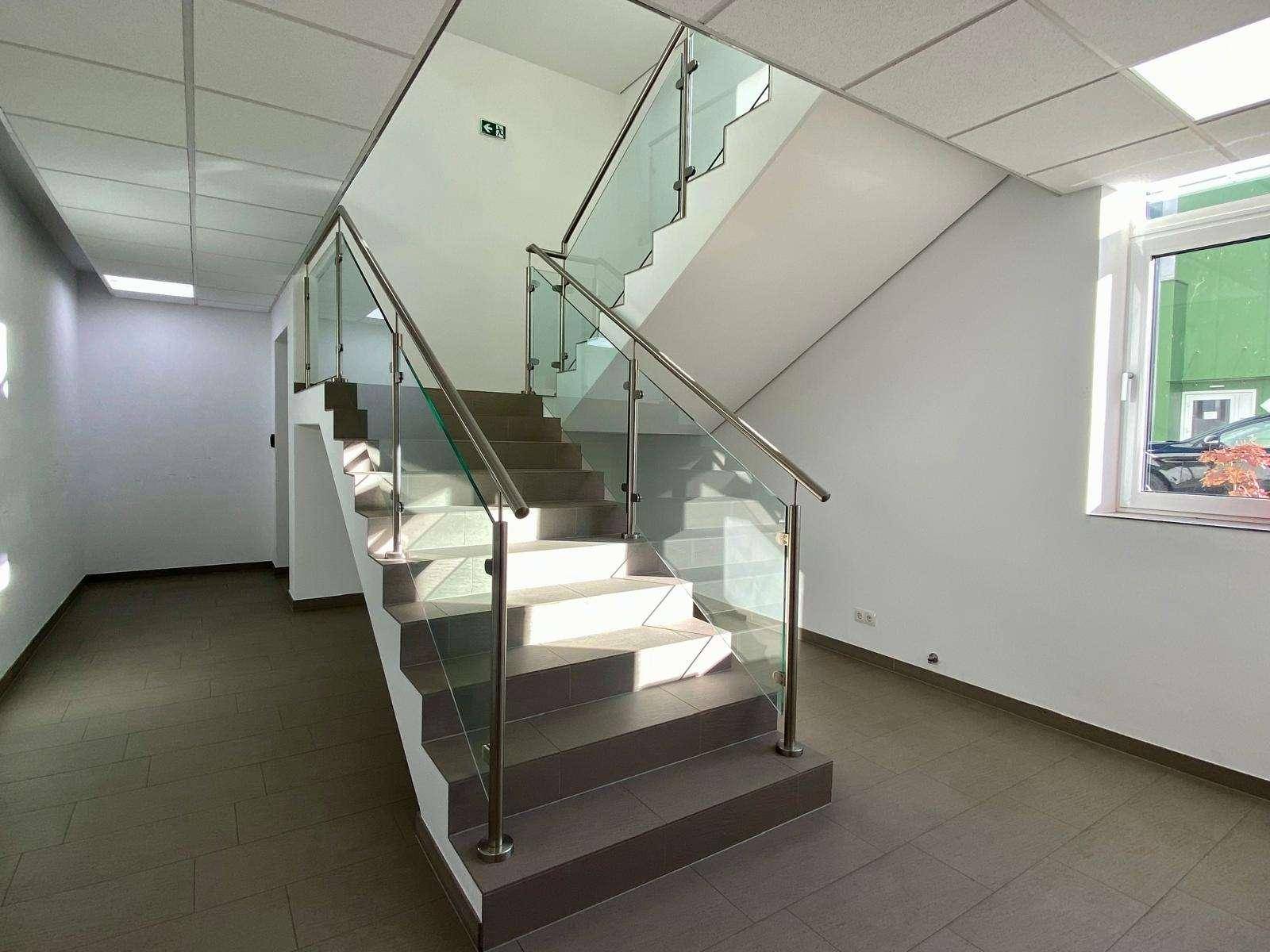 Moderne Treppe mit Glasgeländer und Edelstahlhandläufen, die die verschiedenen Etagen des Gebäudes verbindet.
