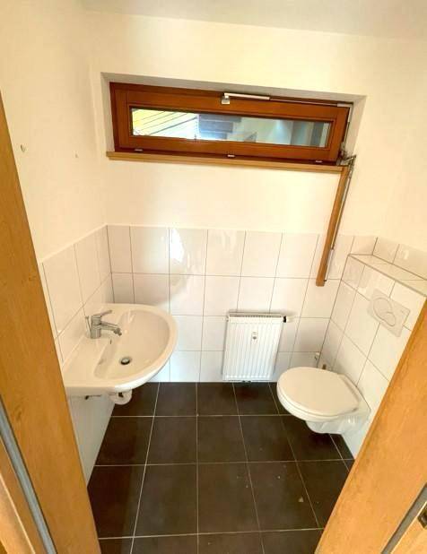 Kleines Gäste-WC mit Fenster, Waschbecken und Wand-WC.