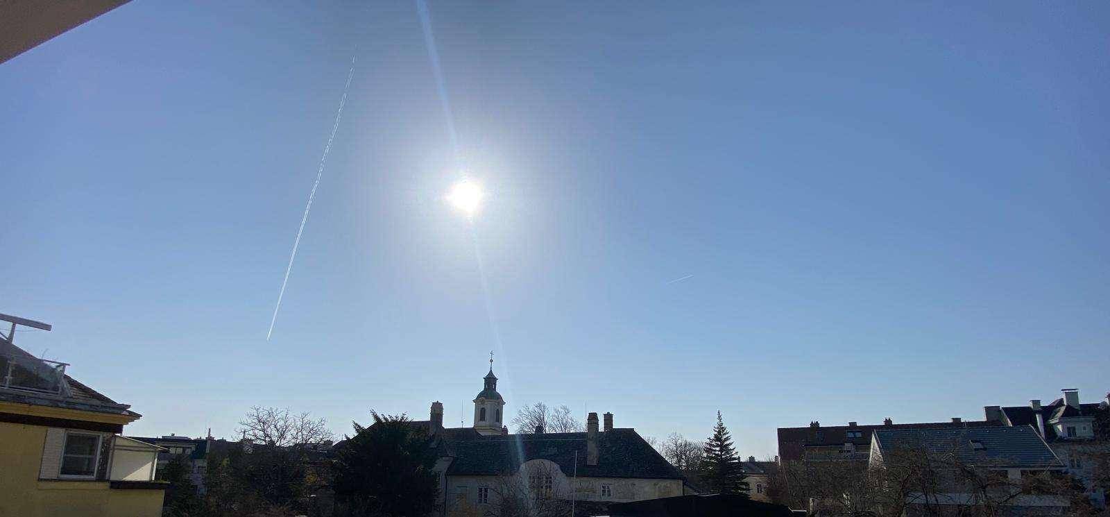 Sonniger Himmel über den Dächern der Stadt mit einem Kirchturm in der Ferne.