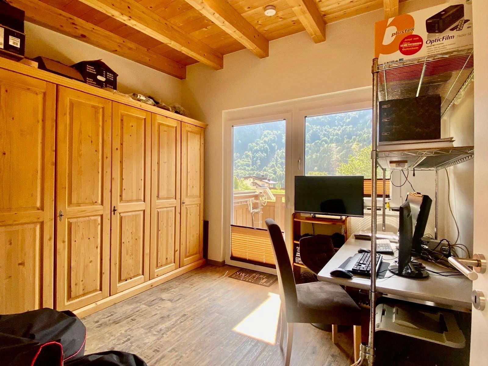 Helles Arbeitszimmer mit großem Holzschrank, Schreibtisch und Zugang zum Balkon.