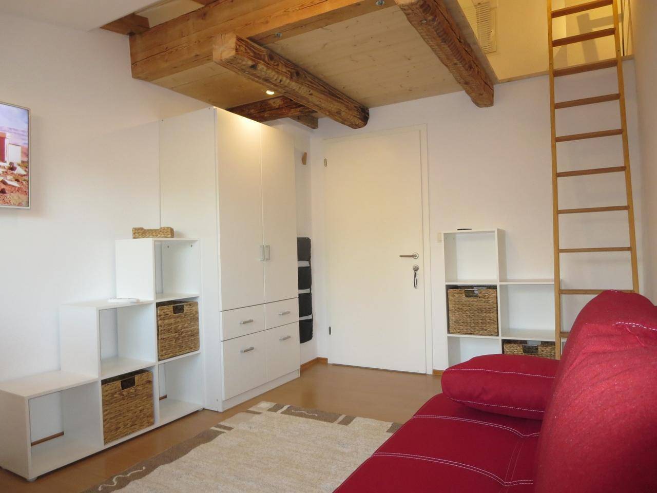 Kleiderschrank und Zugang zu einem Hochbett über eine Holzleiter in einem hellen Raum.