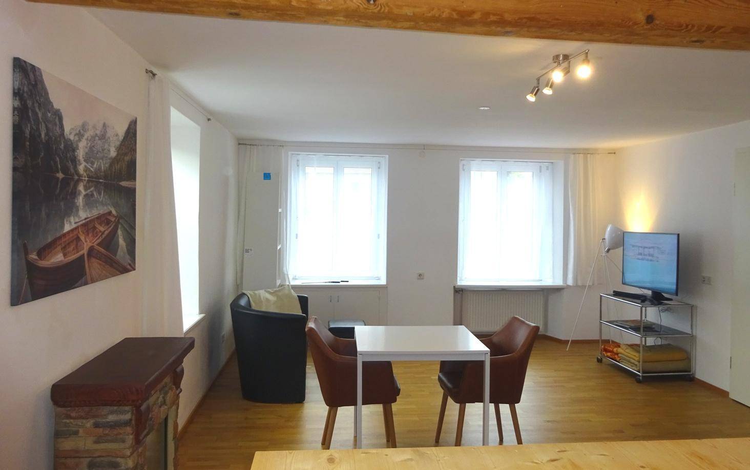 Gemütlicher Wohnbereich mit Esstisch, Fernseher und zwei Fenstern, ergänzt durch einen Kamin.