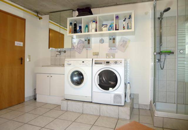 Praktischer Hauswirtschaftsraum mit Waschmaschine, Trockner, Waschbecken und Duschkabine.