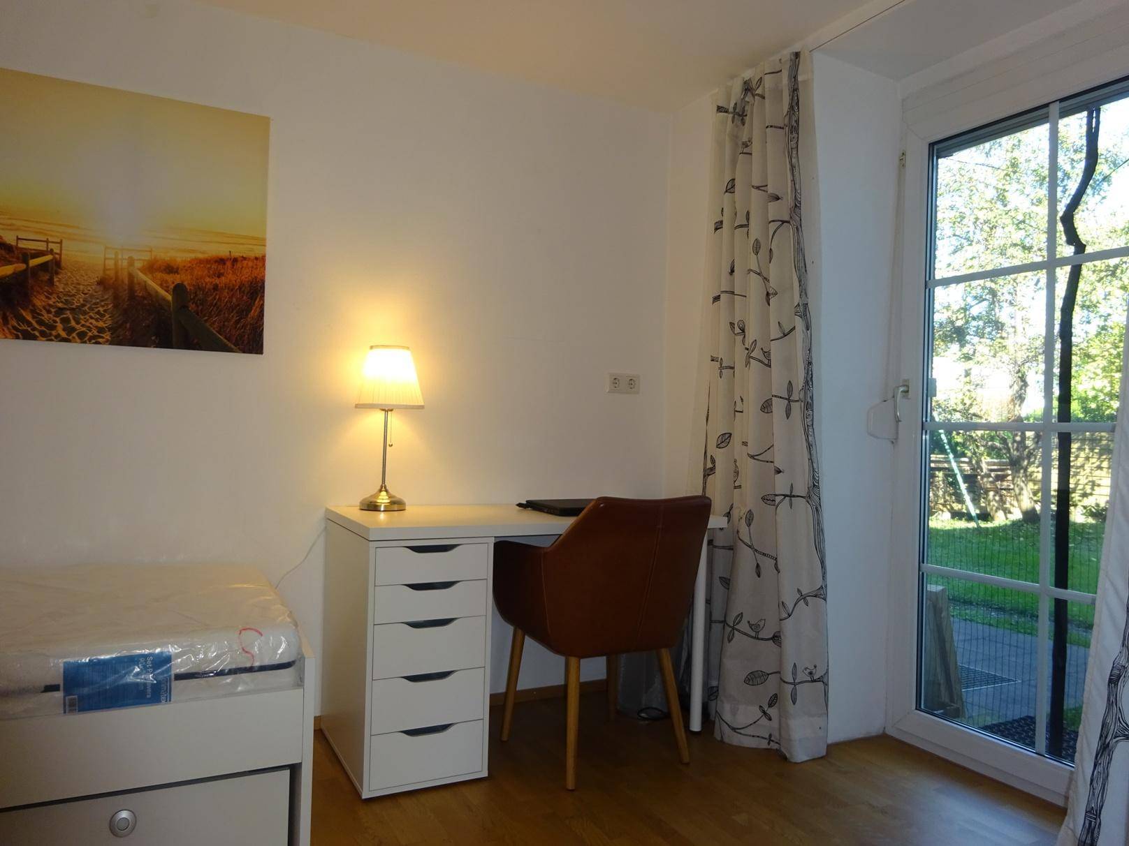 Schlafzimmer mit Schreibtisch, Stuhl und großem Fenster, das Zugang zum Außenbereich bietet.