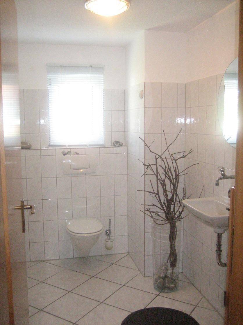 Modernes Gäste-WC mit weißen Fliesen, wandhängender Toilette und einem Fenster.