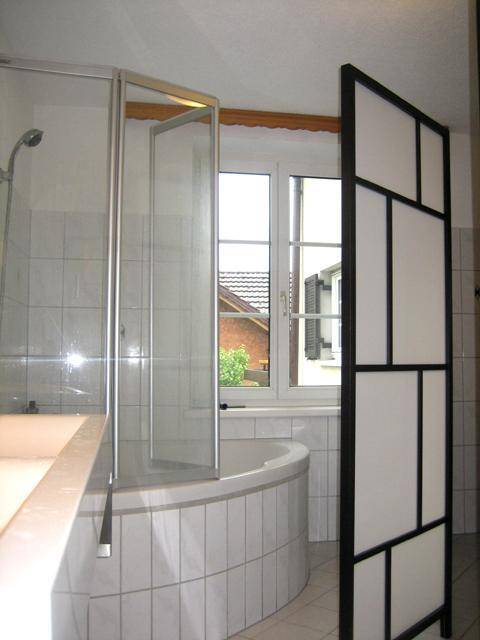 Badezimmer mit Eckbadewanne, Duschabtrennung und Fenster, alles in hellen Fliesen gehalten.