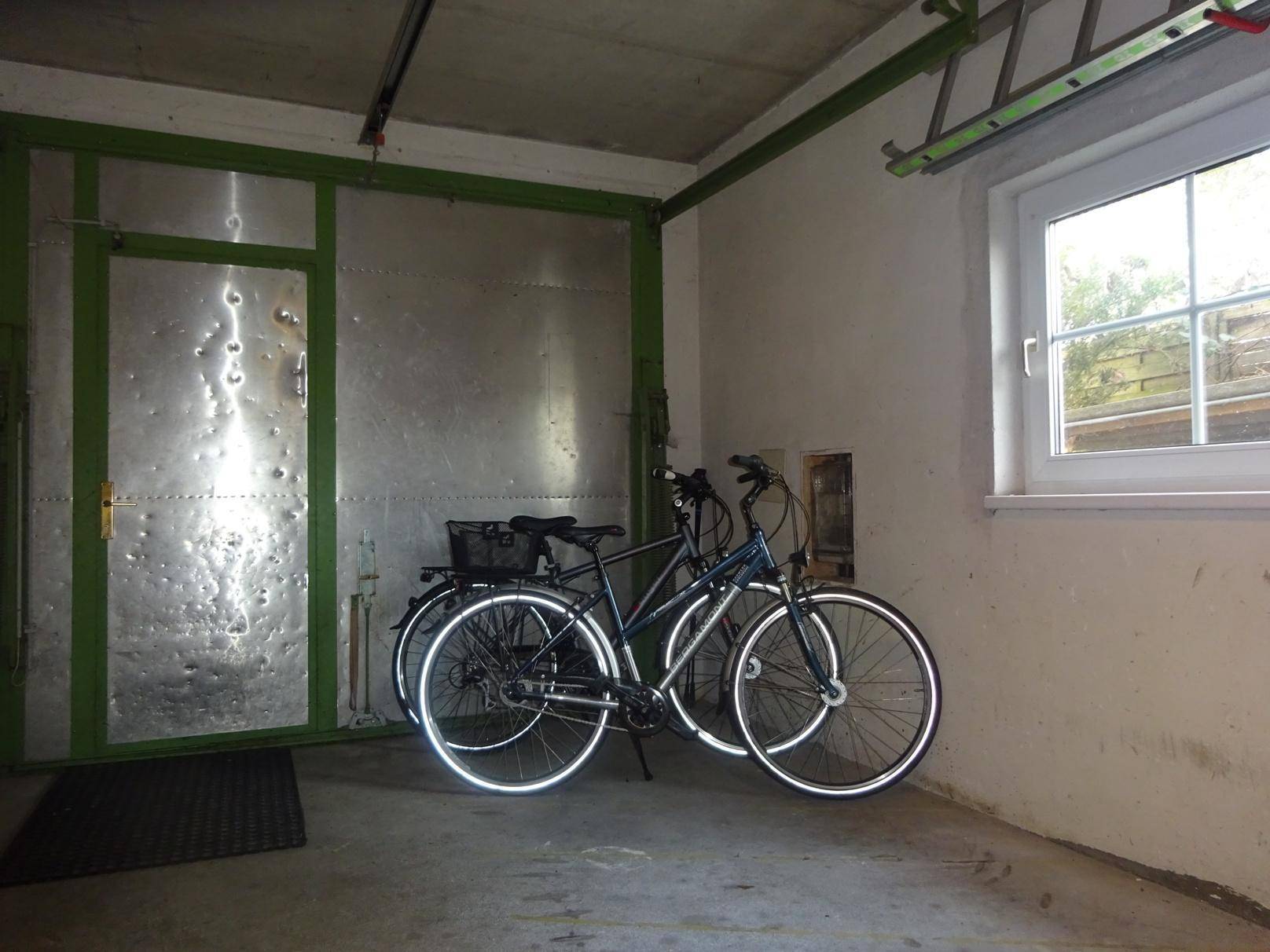 Geräumige Garage mit zwei Fahrrädern, einem Fenster und einer Metalltür.