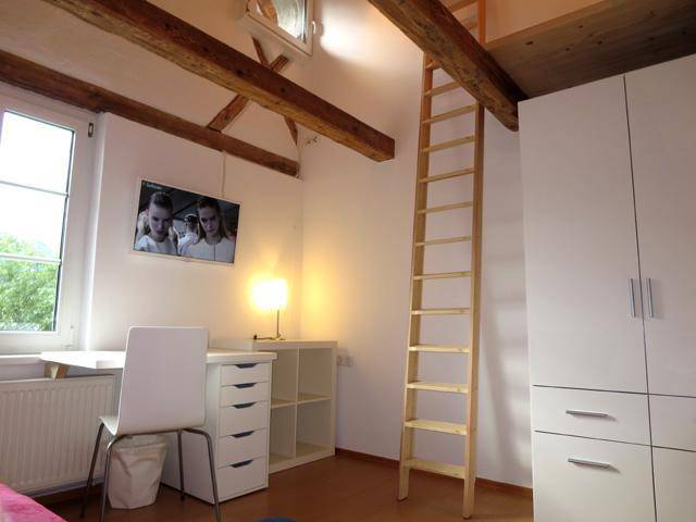 Schlafzimmer mit Kleiderschrank, Schreibtisch und Leiter, die zu einem oberen Schlafbereich führt.