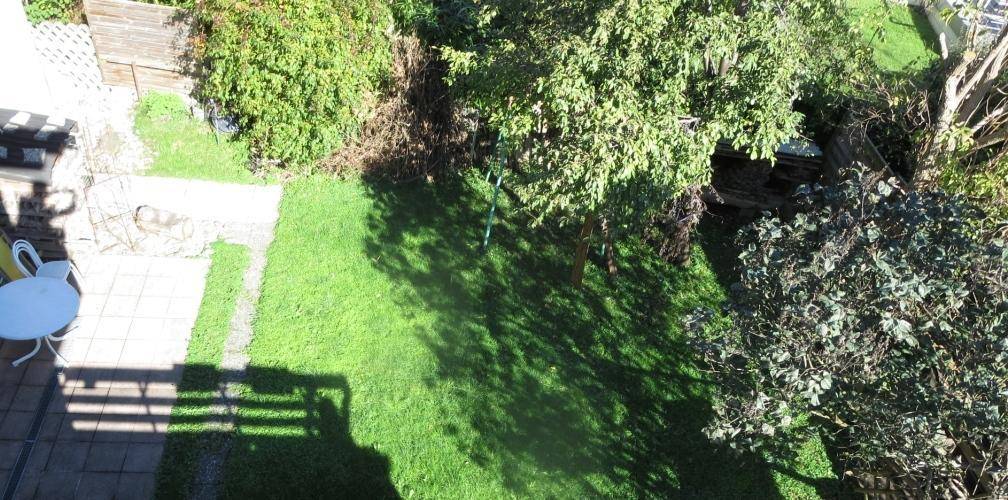 Grüner Garten mit Rasenfläche, Bäumen und einer gepflasterten Terrasse mit Sitzgelegenheiten.