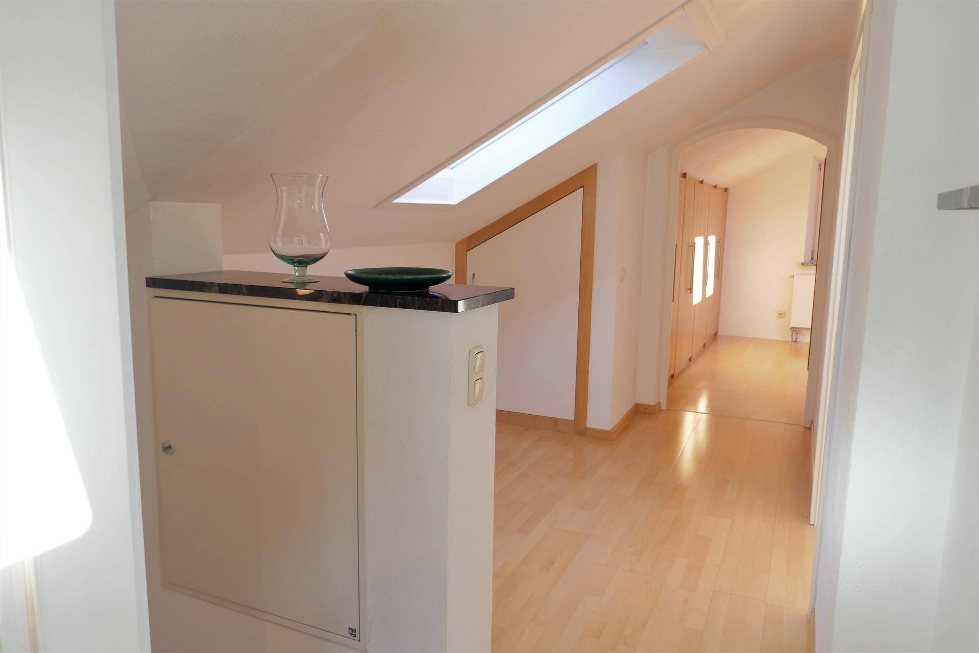 Heller Flur im Dachgeschoss mit Dachfenster und Holzboden, der zu weiteren Räumen führt.