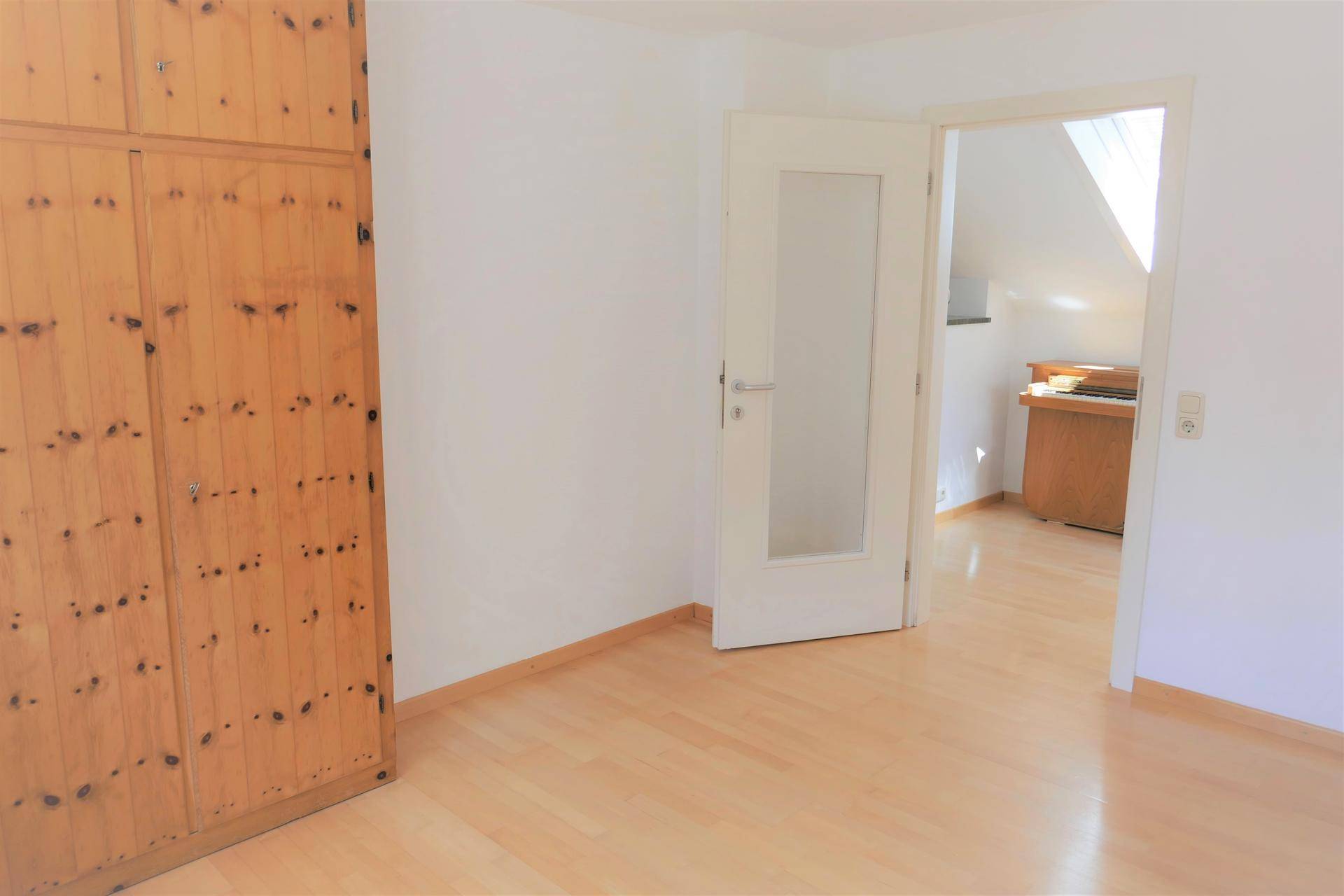 Helles Zimmer mit Holzboden und Zugang zu einem weiteren Raum im Dachgeschoss.