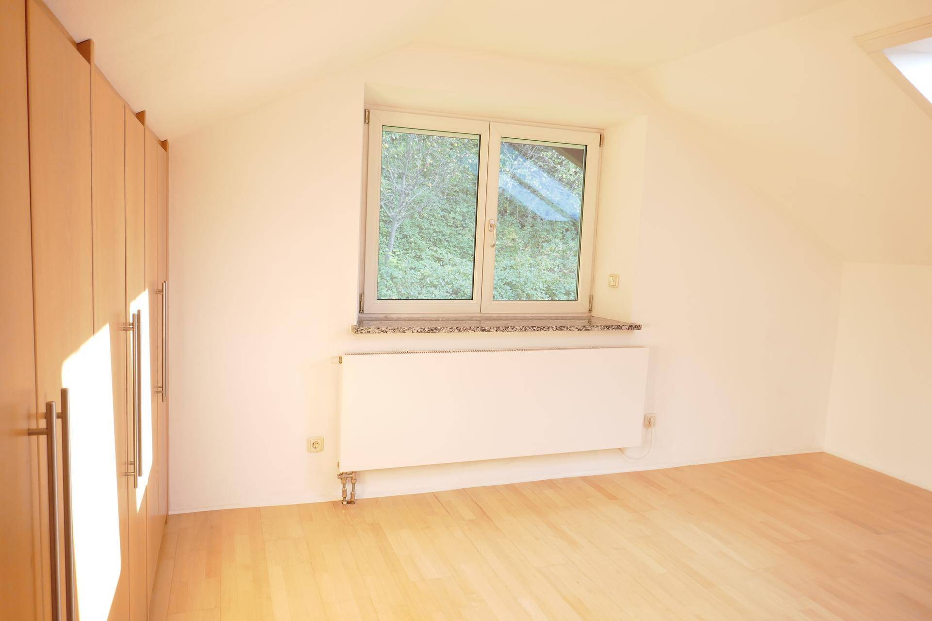 Gemütliches Schlafzimmer im Dachgeschoss mit Einbauschränken und Blick ins Grüne.