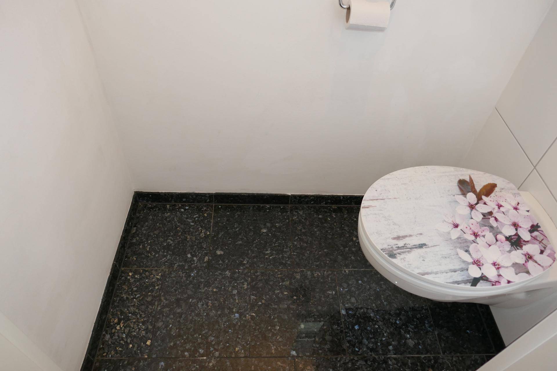 Separate Toilette mit dunklem Fliesenboden und dekorativem Toilettendeckel.
