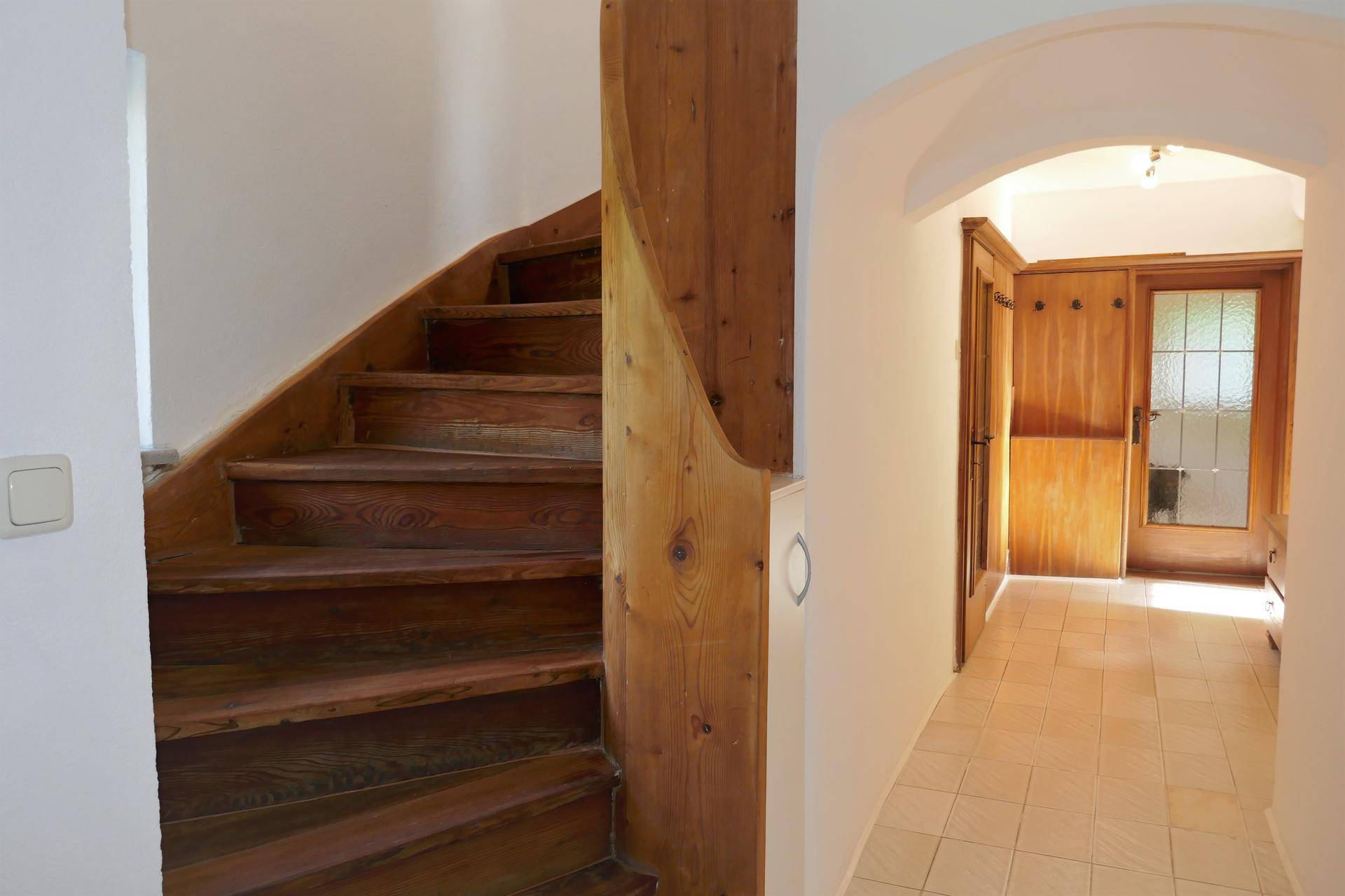 Helle Diele mit Holztreppe und gefliestem Boden, die zu den oberen Etagen führt.