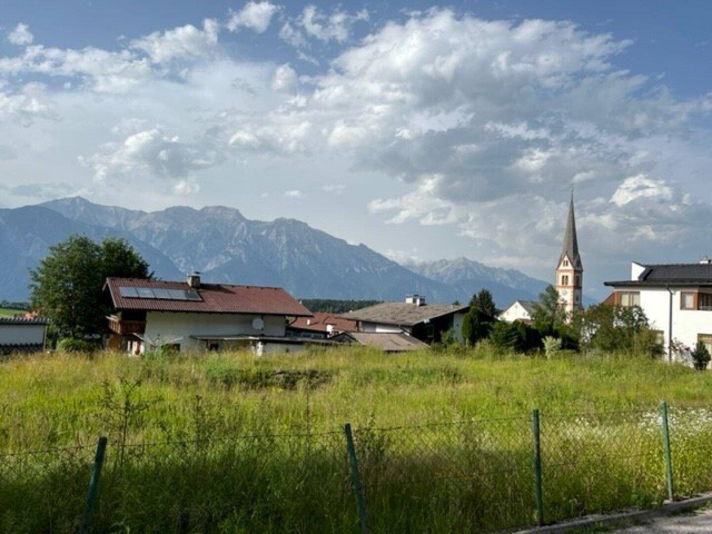 Grünes Baugrundstück mit Panoramablick auf die majestätischen Berge und die Dorfkirche.