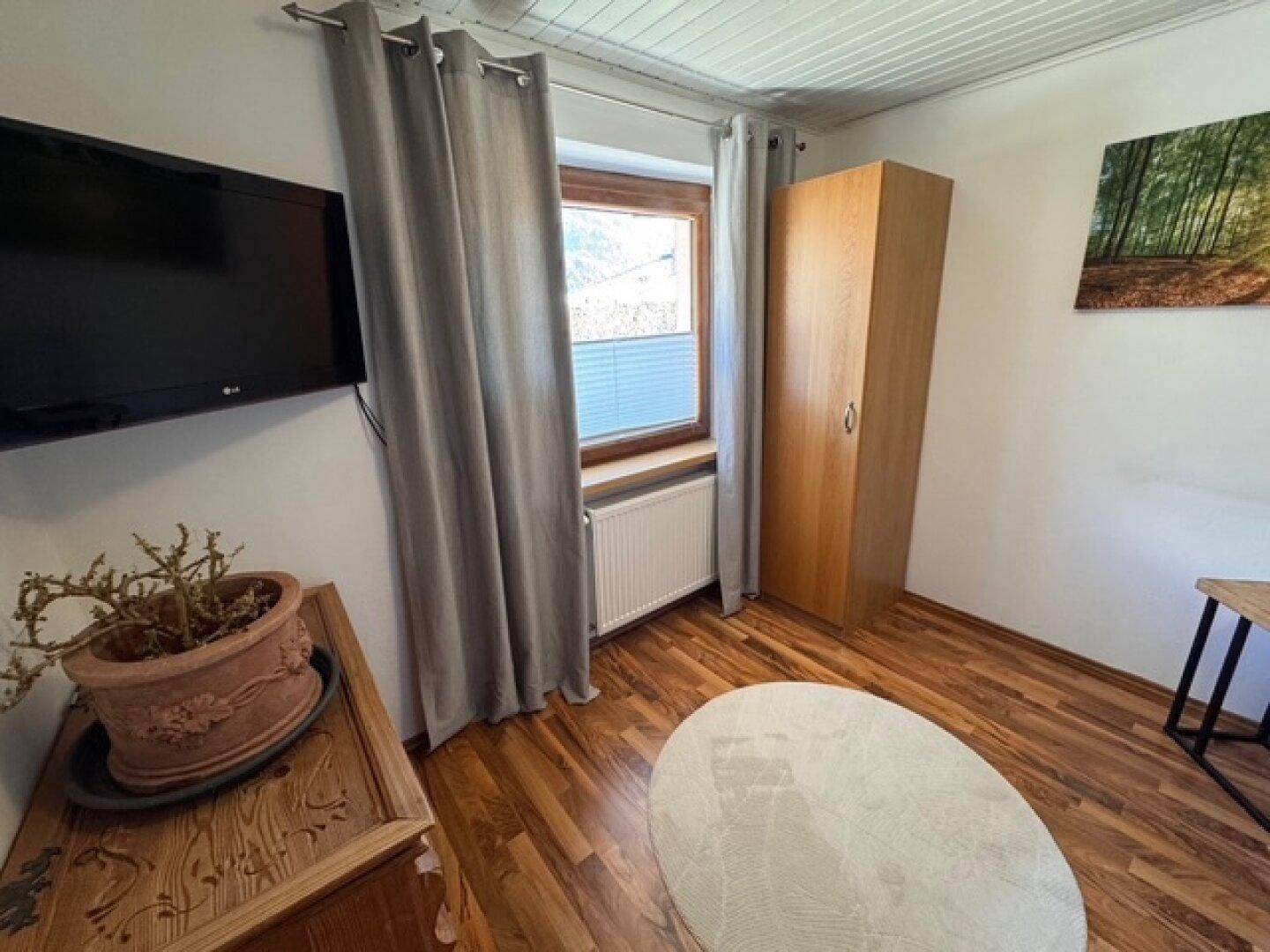 Gemütliches Schlafzimmer mit Holzboden, Kleiderschrank und Fernseher an der Wand.