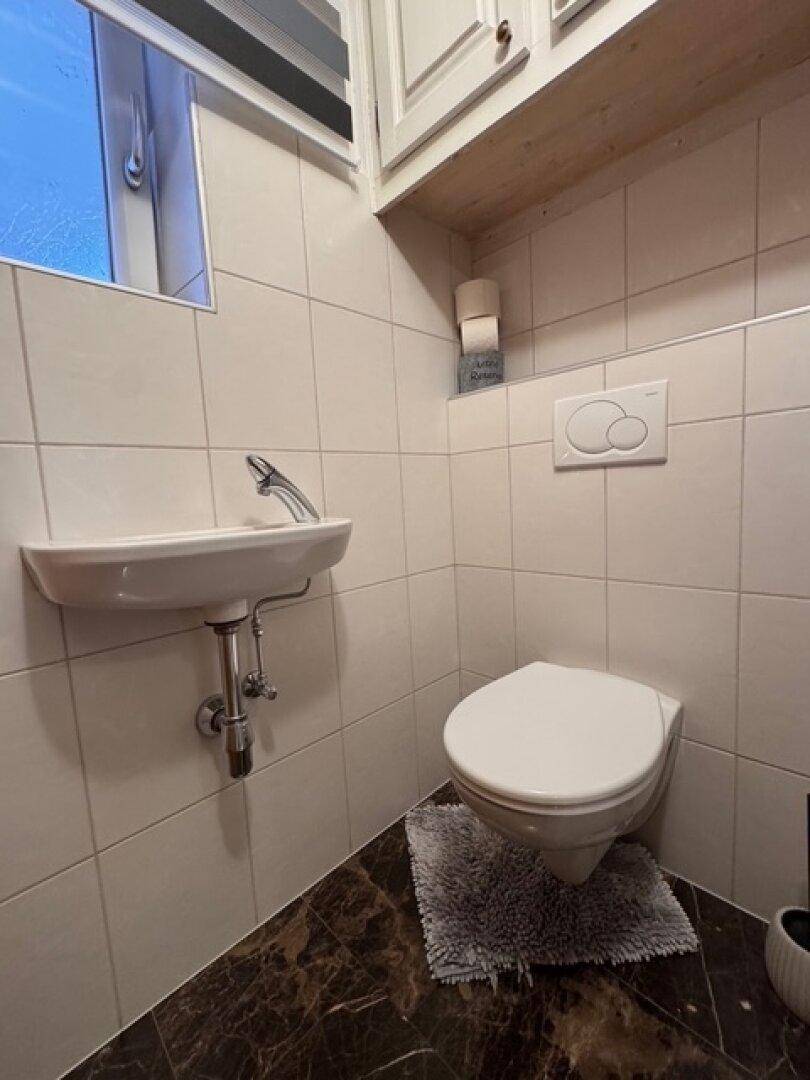 Kleines Gäste-WC mit wandhängendem WC, Handwaschbecken und Fenster.