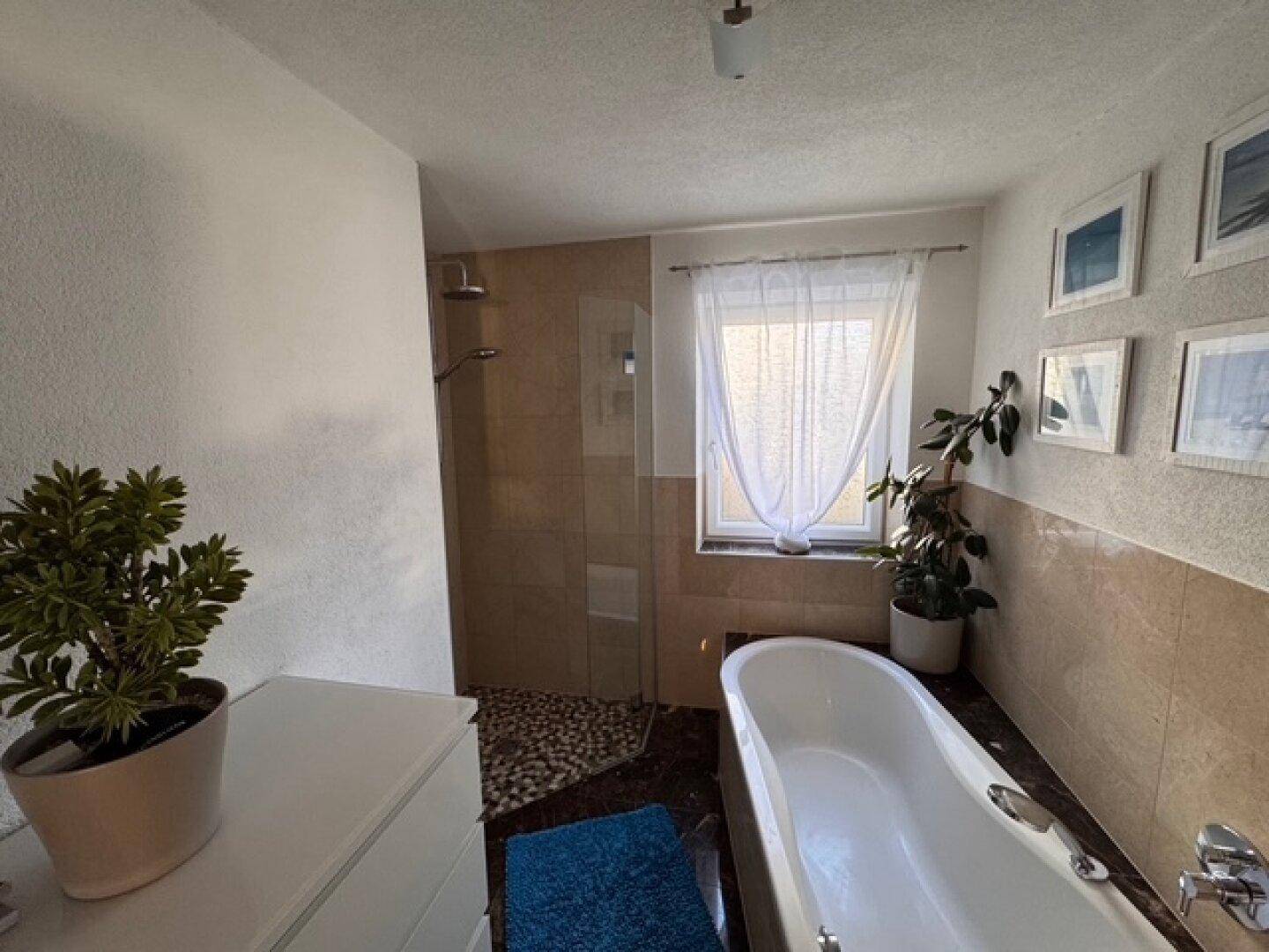 Helles Badezimmer mit Badewanne, Dusche, Einzelwaschbecken und Fenster.