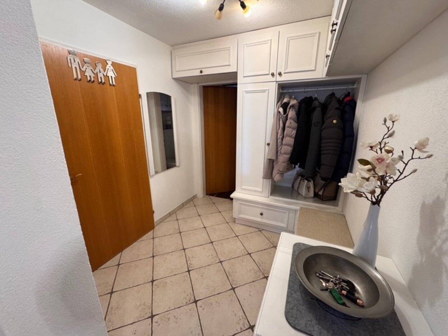 Heller Flur mit integrierter Garderobe, weißem Einbauschrank und Fliesenboden.