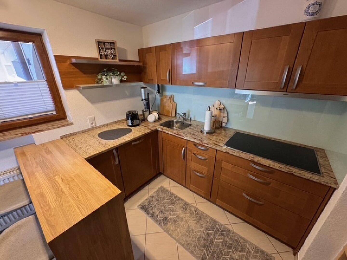 Küche mit Holzschränken, Granitarbeitsplatte, Spüle und Kochfeld.