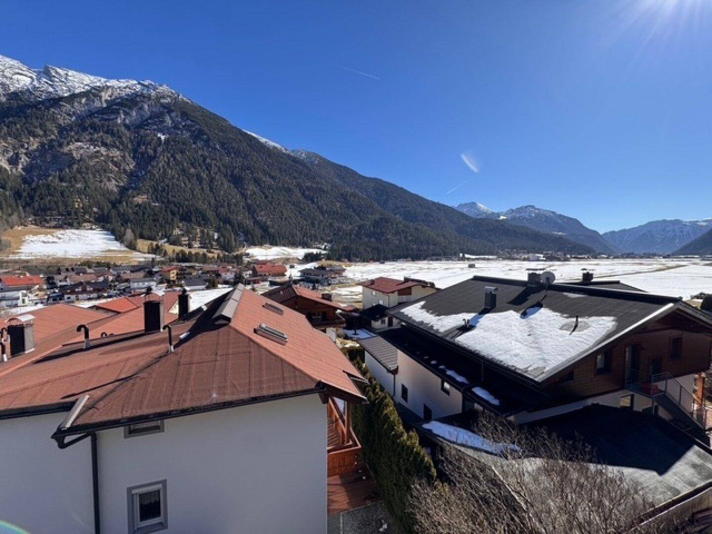 Panoramablick über ein alpines Dorf mit vielen Dächern und schneebedeckten Bergen.