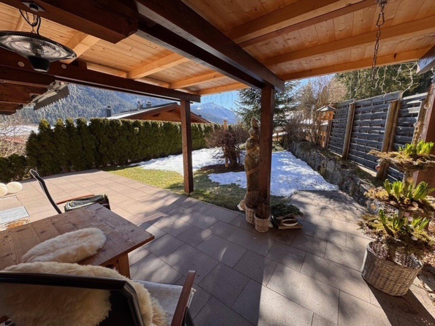 Überdachte Terrasse mit Sitzgelegenheiten, Blick auf den Garten und die verschneiten Berge.