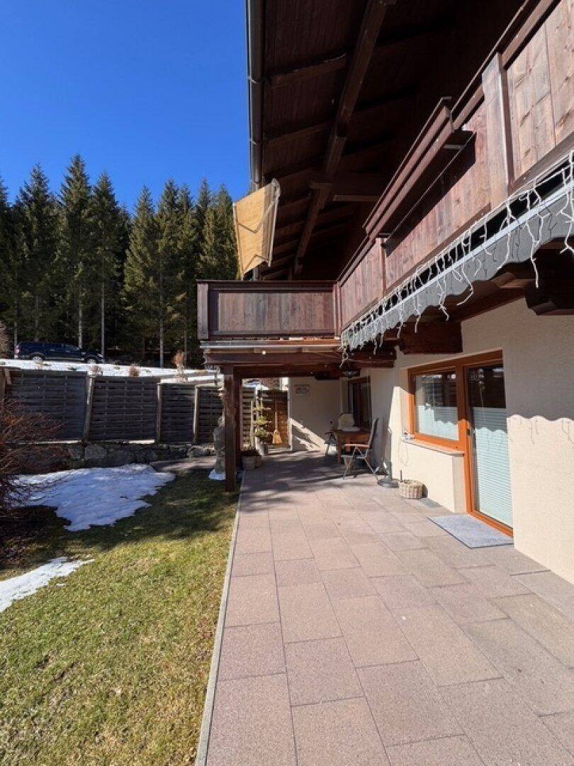 Außenbereich mit gepflasterter Terrasse, Rasenfläche und angrenzendem Wald im Winter.