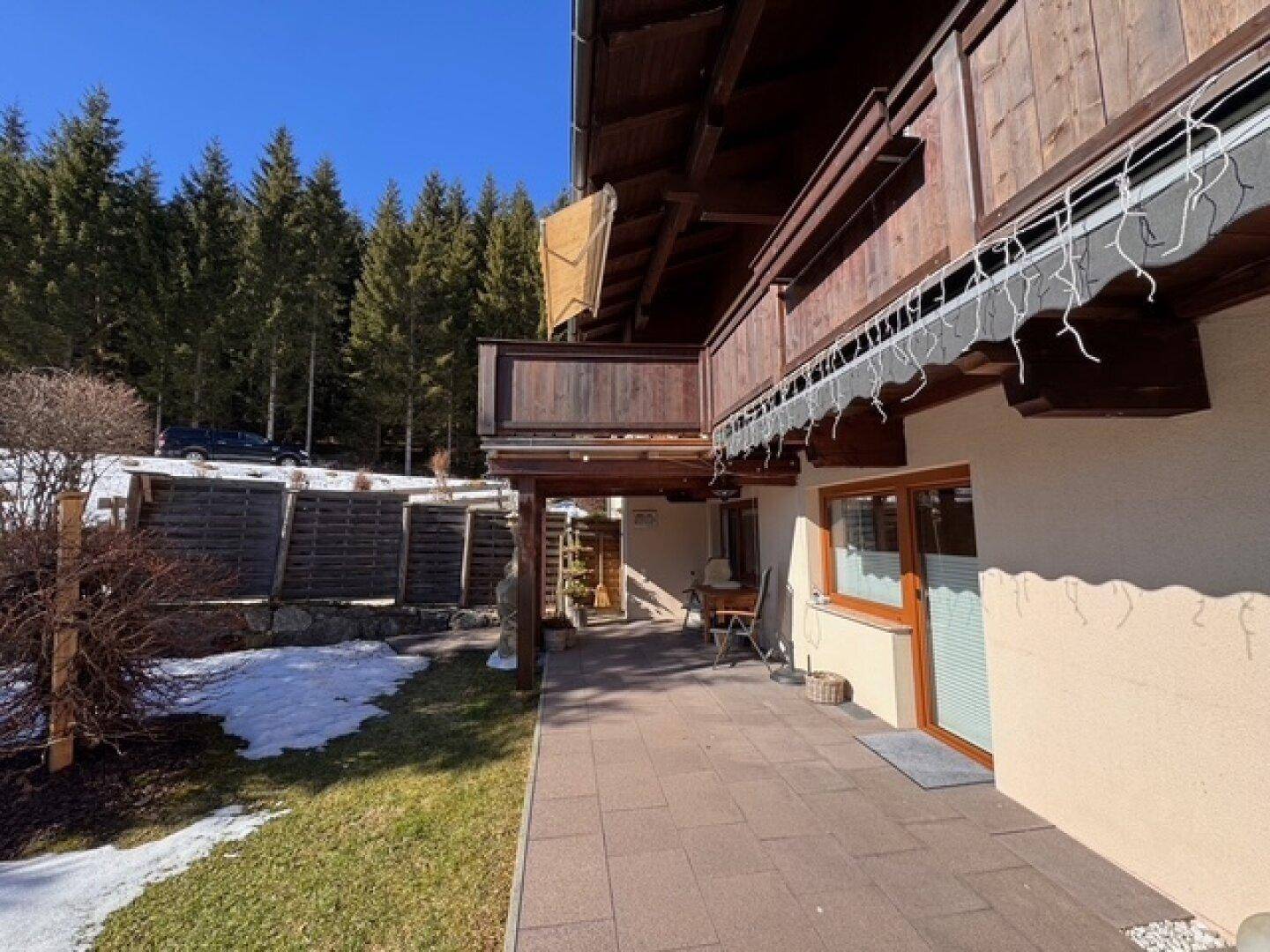 Gepflasterte Terrasse am Haus mit Zugang zum Garten und Blick auf die umliegenden Bäume.