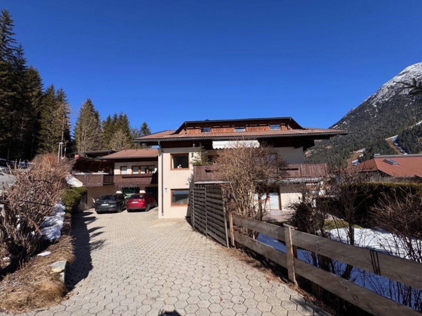 Einfamilienhaus mit gepflasterter Auffahrt und Bergblick, umgeben von Bäumen und Schnee.