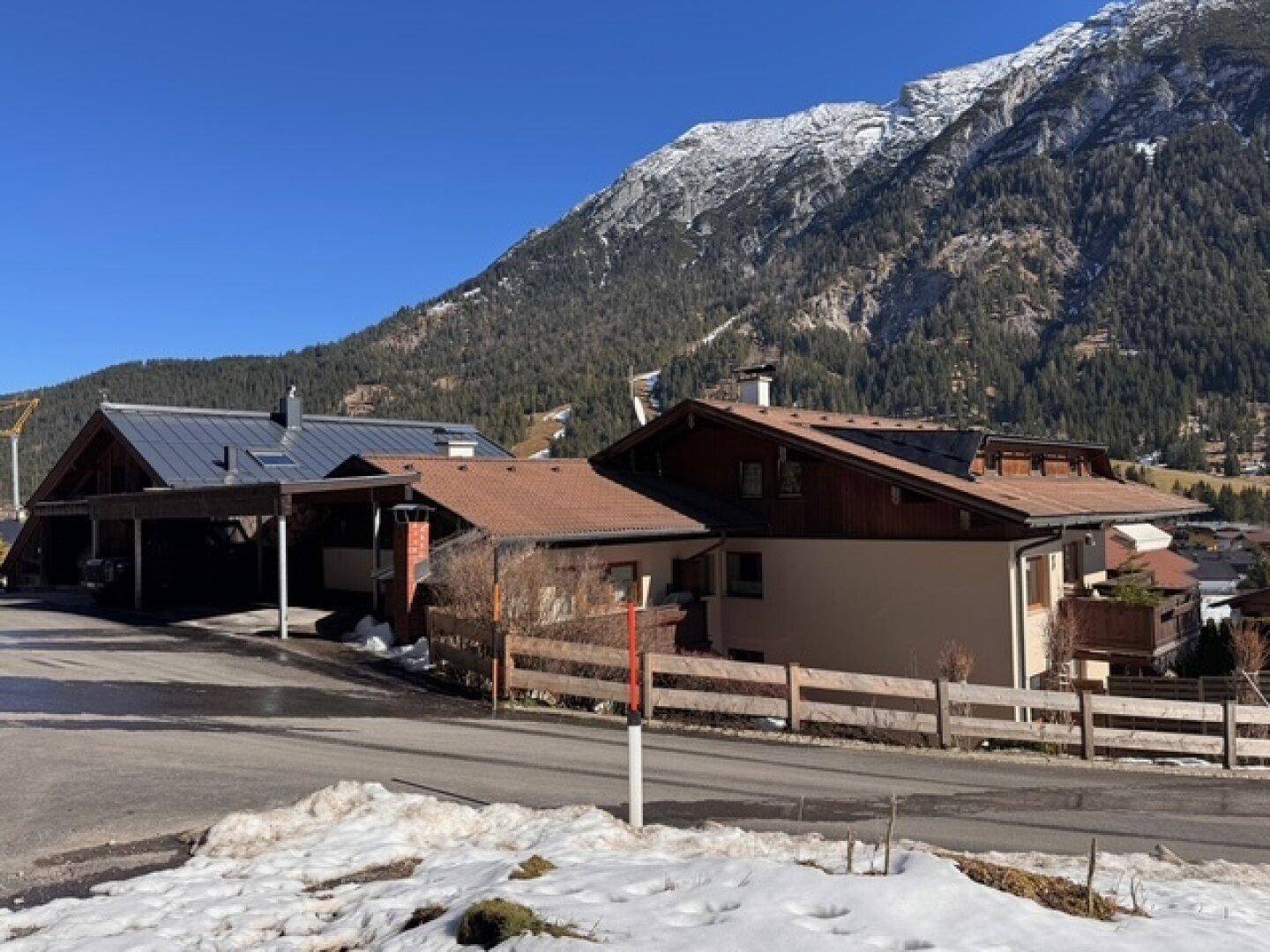 Mehrere Wohnhäuser in alpiner Umgebung mit schneebedeckten Bergen im Hintergrund.