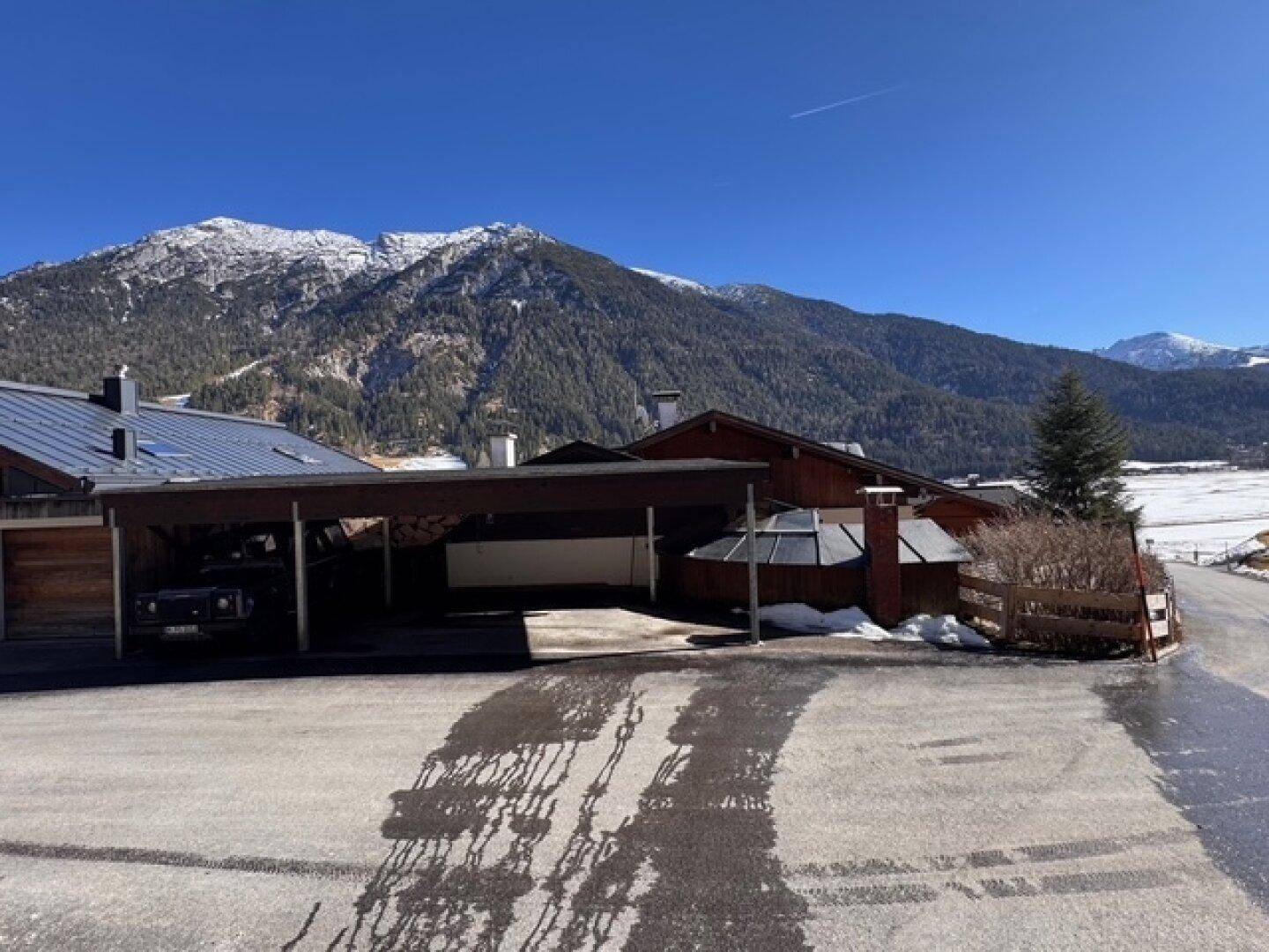 Carport und Außenbereich eines Hauses mit schneebedeckten Bergen im Hintergrund.