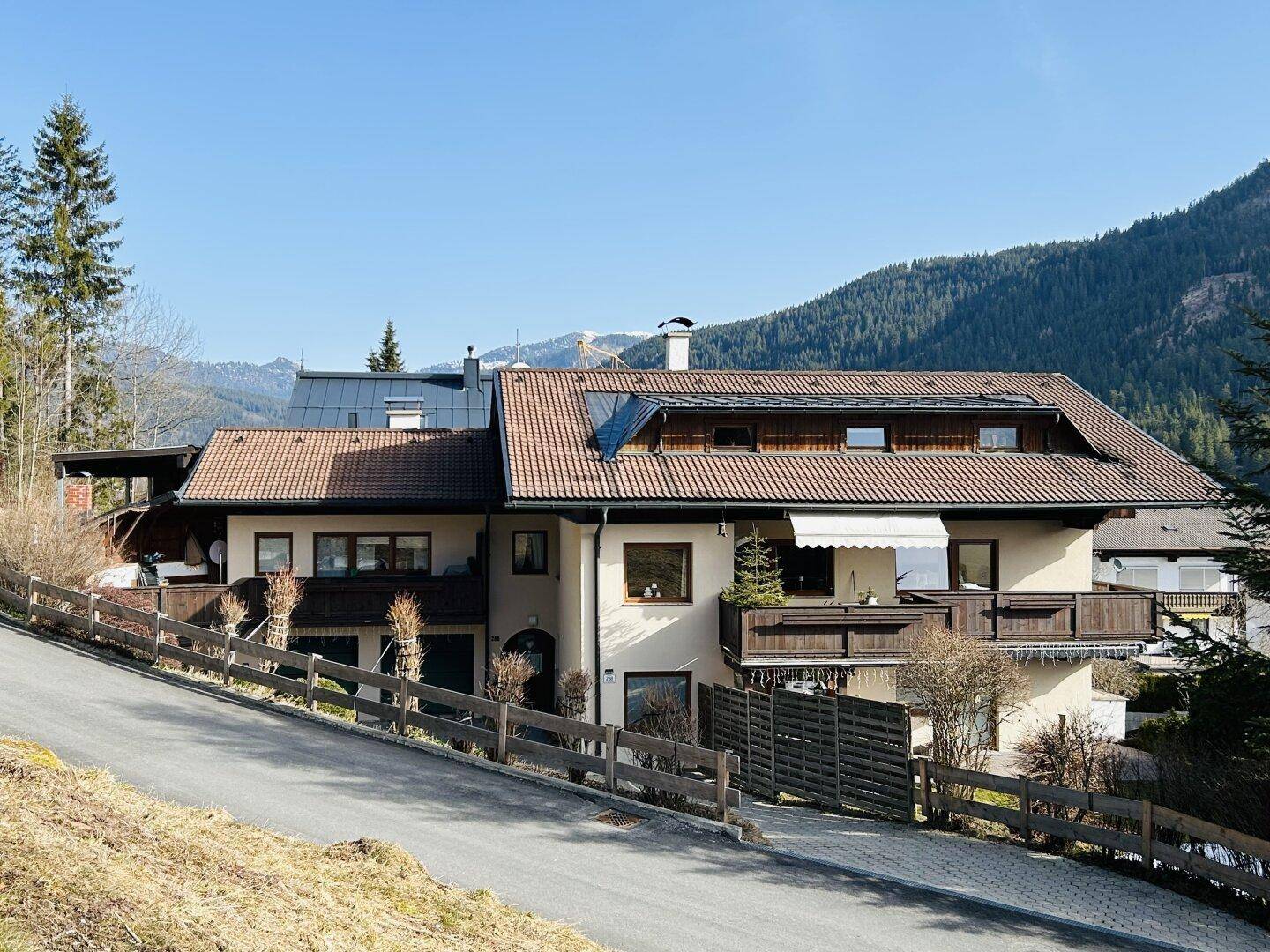Wohnhaus in alpiner Umgebung mit Ziegeldach, Balkonen und Photovoltaikanlage auf dem Dach.