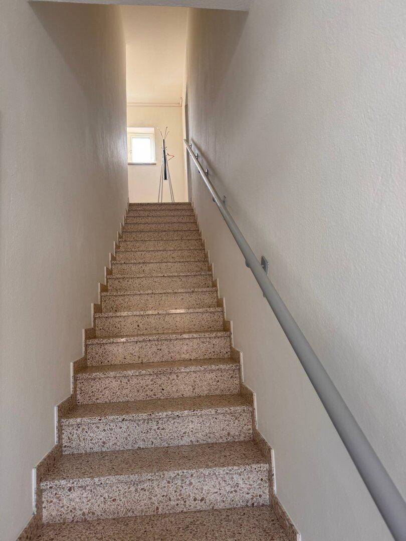 Treppenhaus mit Terrazzo-Stufen, einem Handlauf und einem kleinen Fenster am oberen Ende.