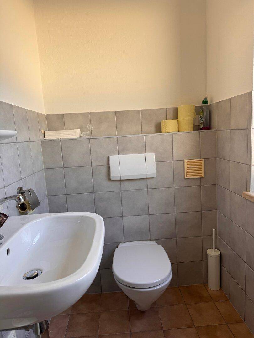 Kleines Badezimmer mit WC, Waschbecken, grauen Fliesen und einem Fenster für natürliche Belüftung.