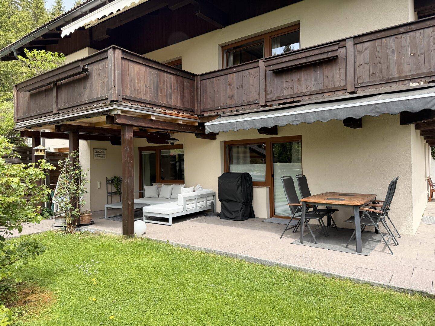 Gemütliche Terrasse mit Essbereich und Lounge-Möbeln, umgeben von Grün und mit Balkon darüber.