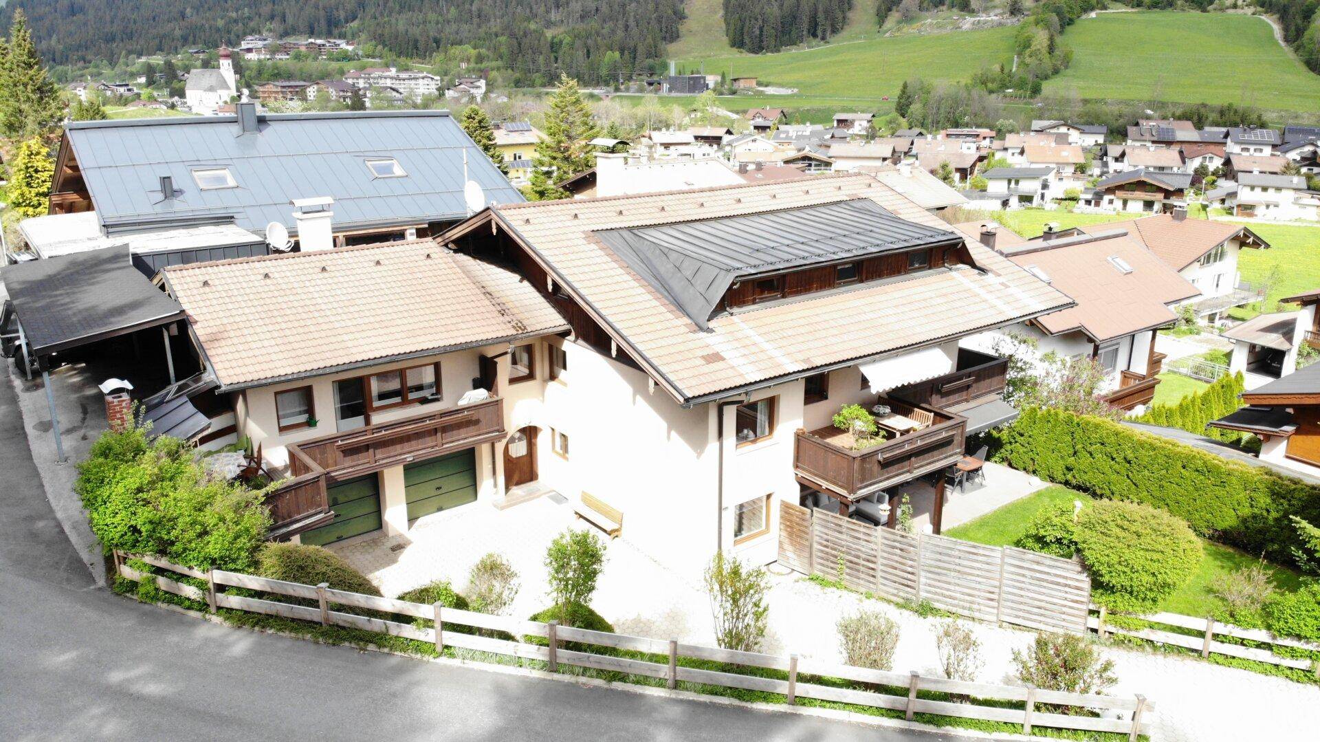 Wohnhaus mit mehreren Balkonen und Satteldach, eingebettet in eine grüne Wohngegend mit Bergblick.