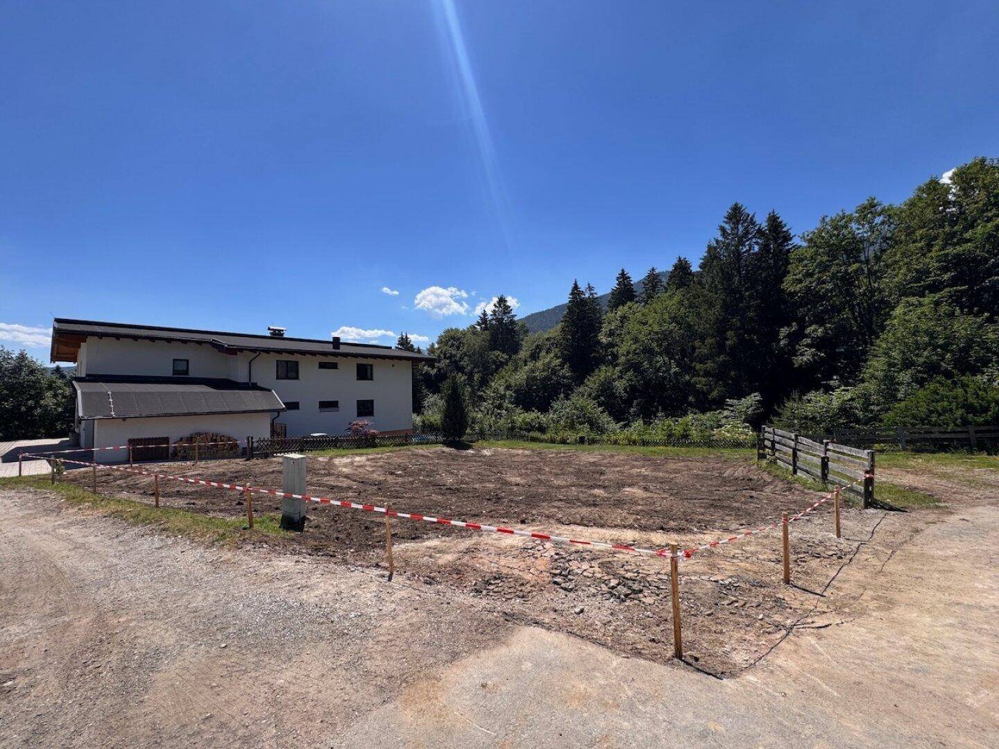 Weitläufiges Grundstück mit Markierungen und einem Gebäude im Hintergrund, umgeben von grüner Natur.