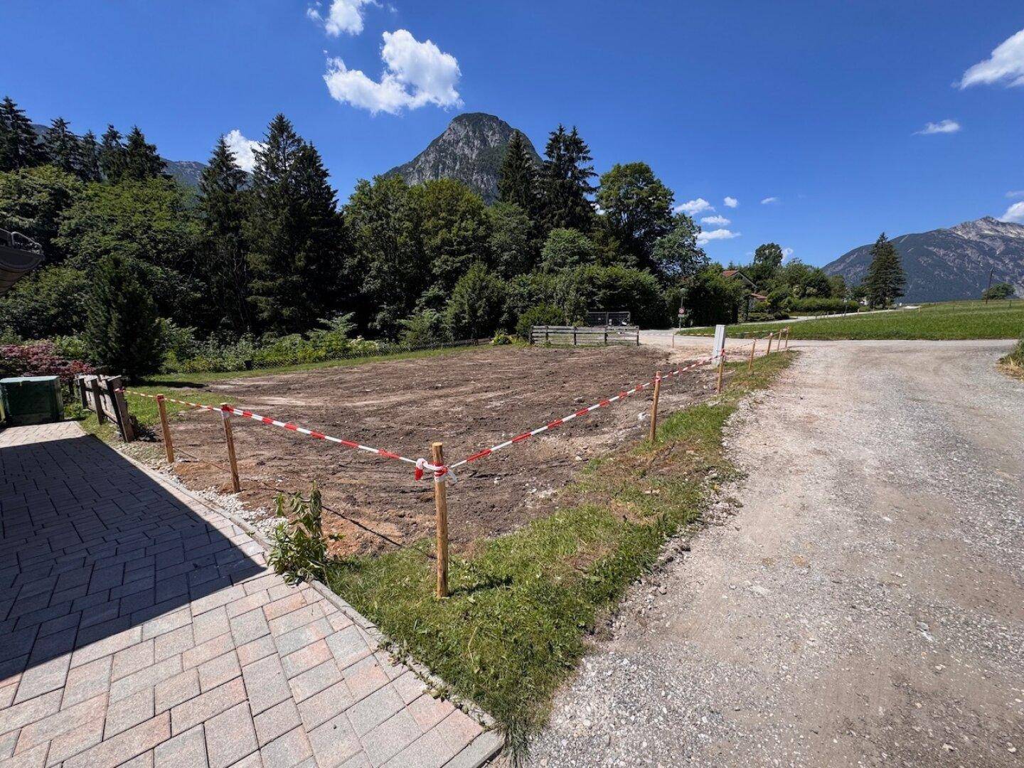 Blick auf das geräumige Grundstück mit Bergblick und angrenzender gepflasterter Fläche.