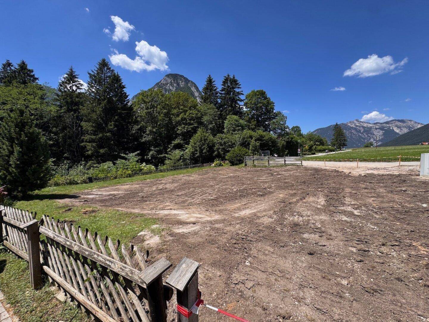 Unbebautes Grundstück umgeben von grünen Bäumen und Bergen, bereit für die Bebauung.