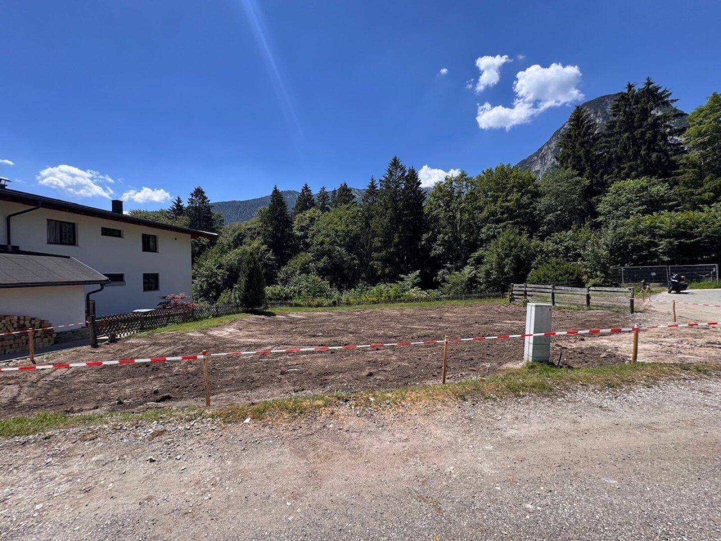 Baugrundstück mit angrenzendem Gebäude und Blick auf die bewaldeten Hänge.