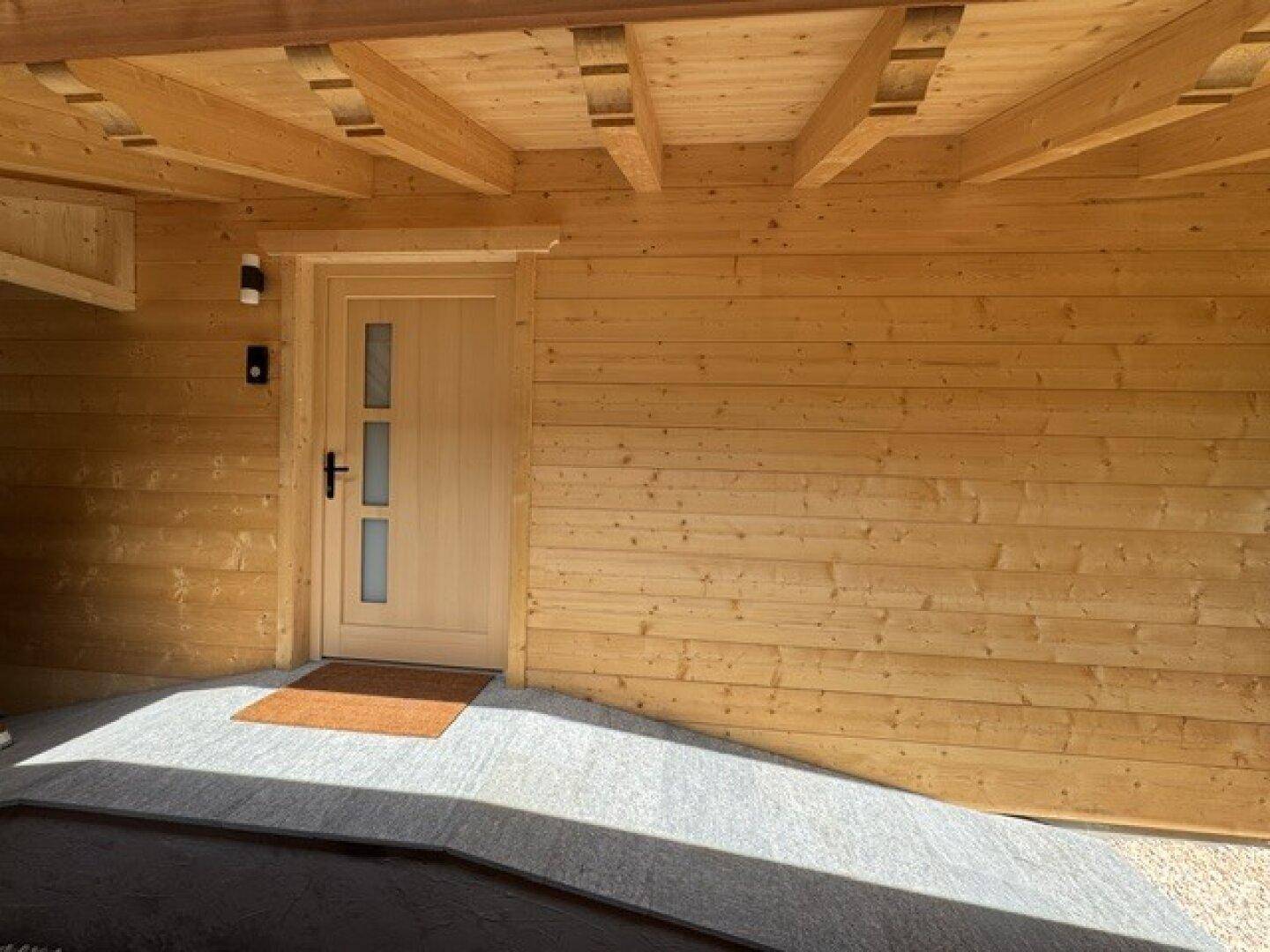 Heller Eingangsbereich mit Holzwänden und moderner Haustür unter dem Carport.