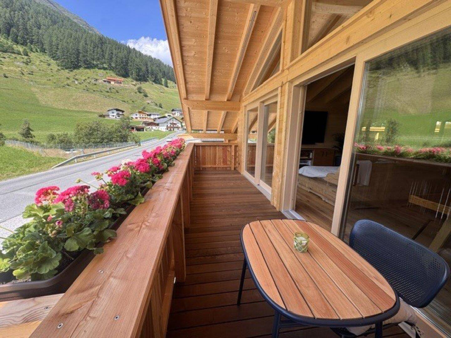 Langer Holzbalkon mit Blumenkästen und Sitzbereich, mit weitem Blick ins Tal.